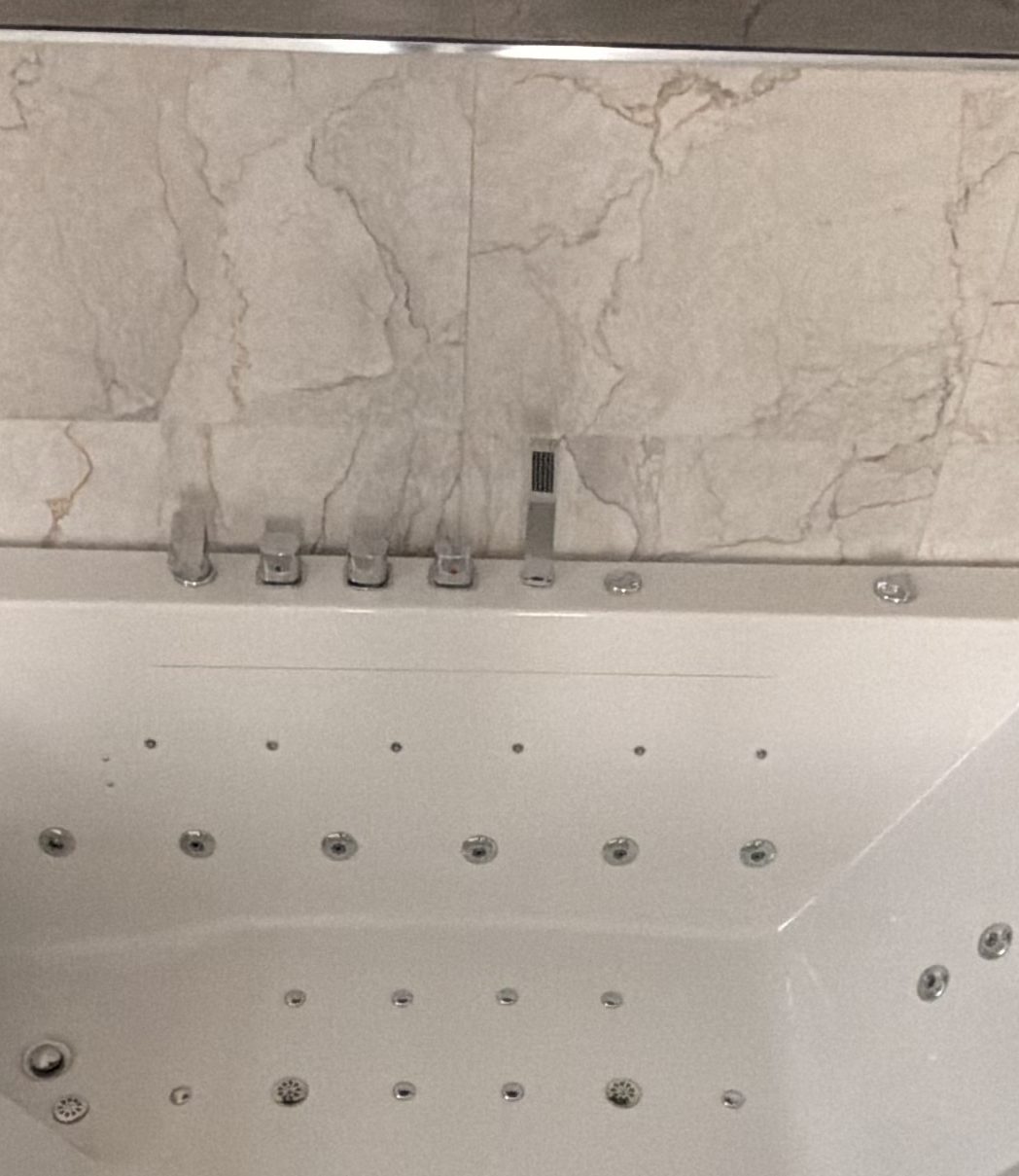 White whirlpool tub with chrome fixtures set in a light marble deck